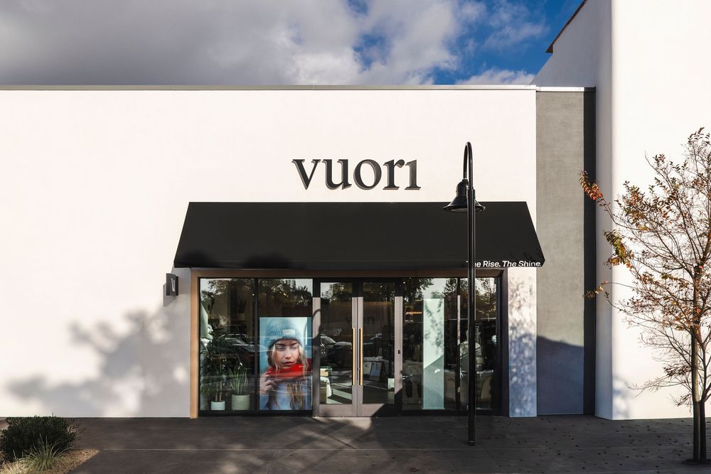 Modern white retail building with glass windows and signage under cloudy sky.