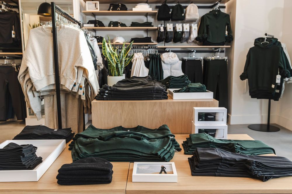 Minimalist retail clothing store interior with racks of neutral-colored garments and modern lighting fixtures.