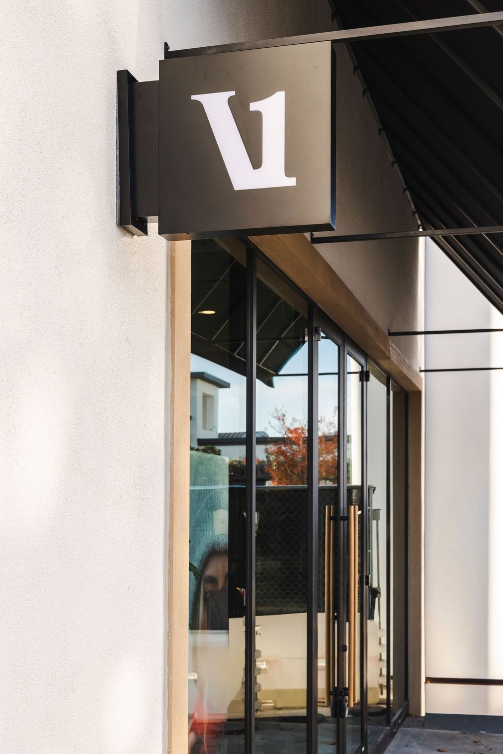 Modern storefront entrance with a minimalist black V1 sign mounted on a white wall above glass doors.