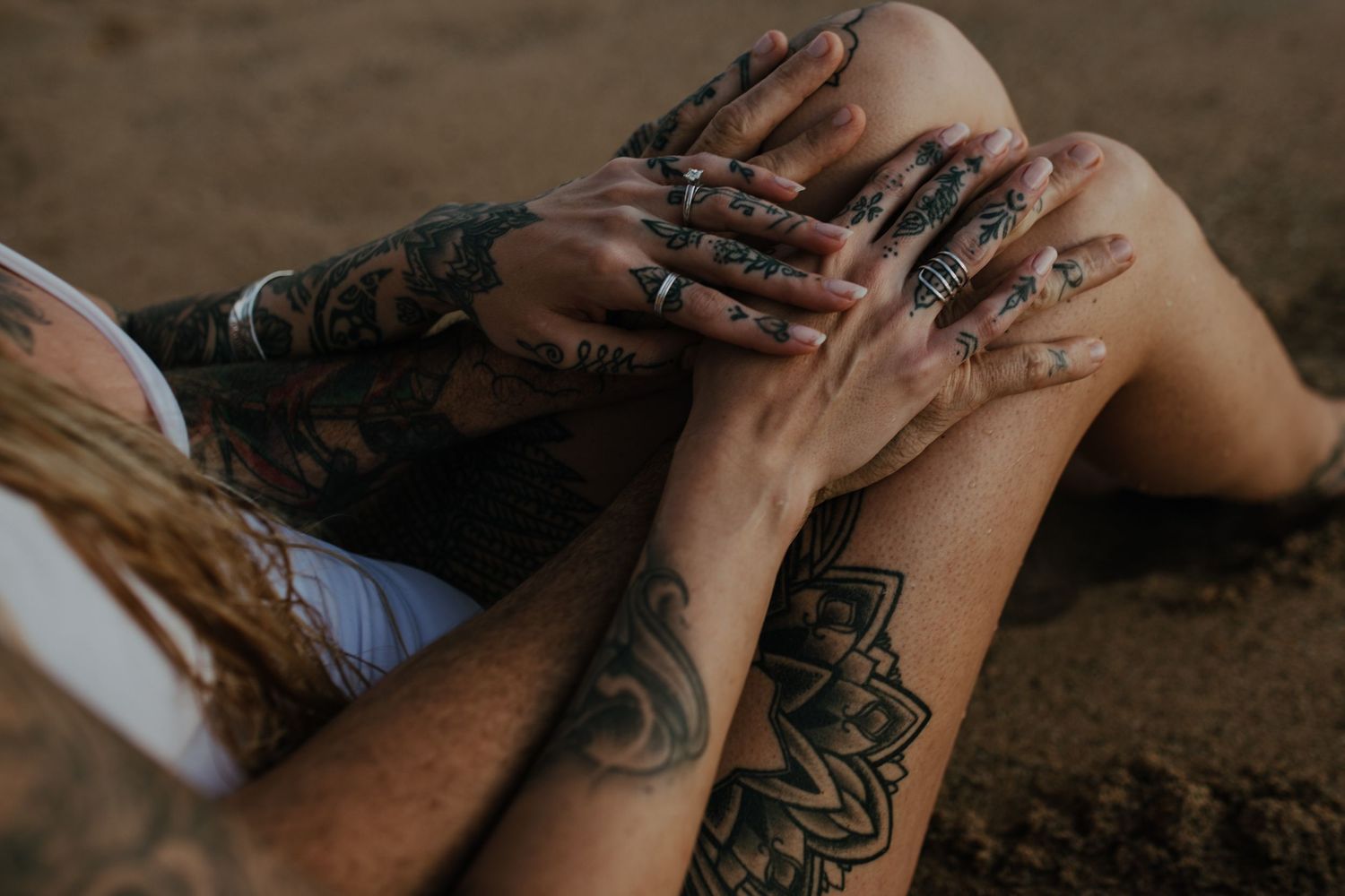 Close-up view of tattooed hands with multiple silver rings against an earthy brown background.