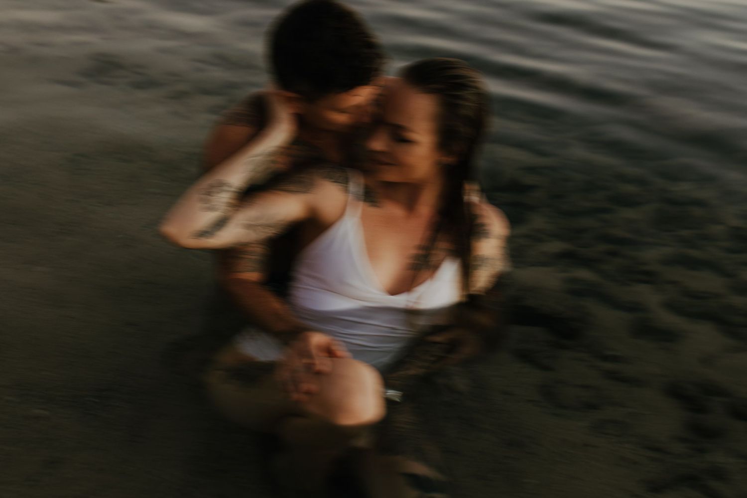 A blurred artistic photo of two people embracing in dark water at dusk.