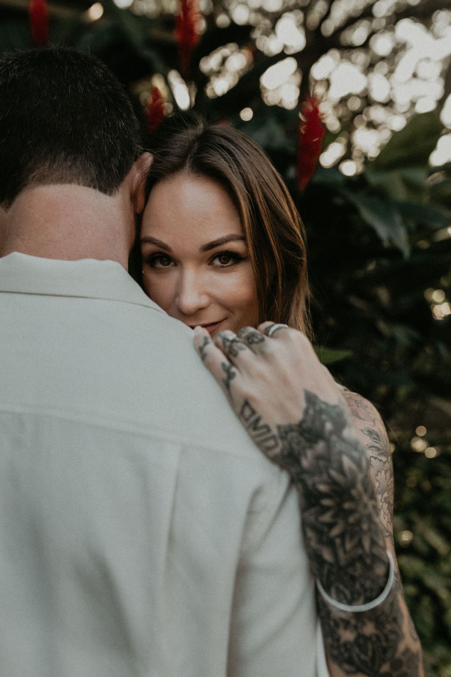An intimate portrait of a couple embracing outdoors with bokeh lights and greenery in the background.