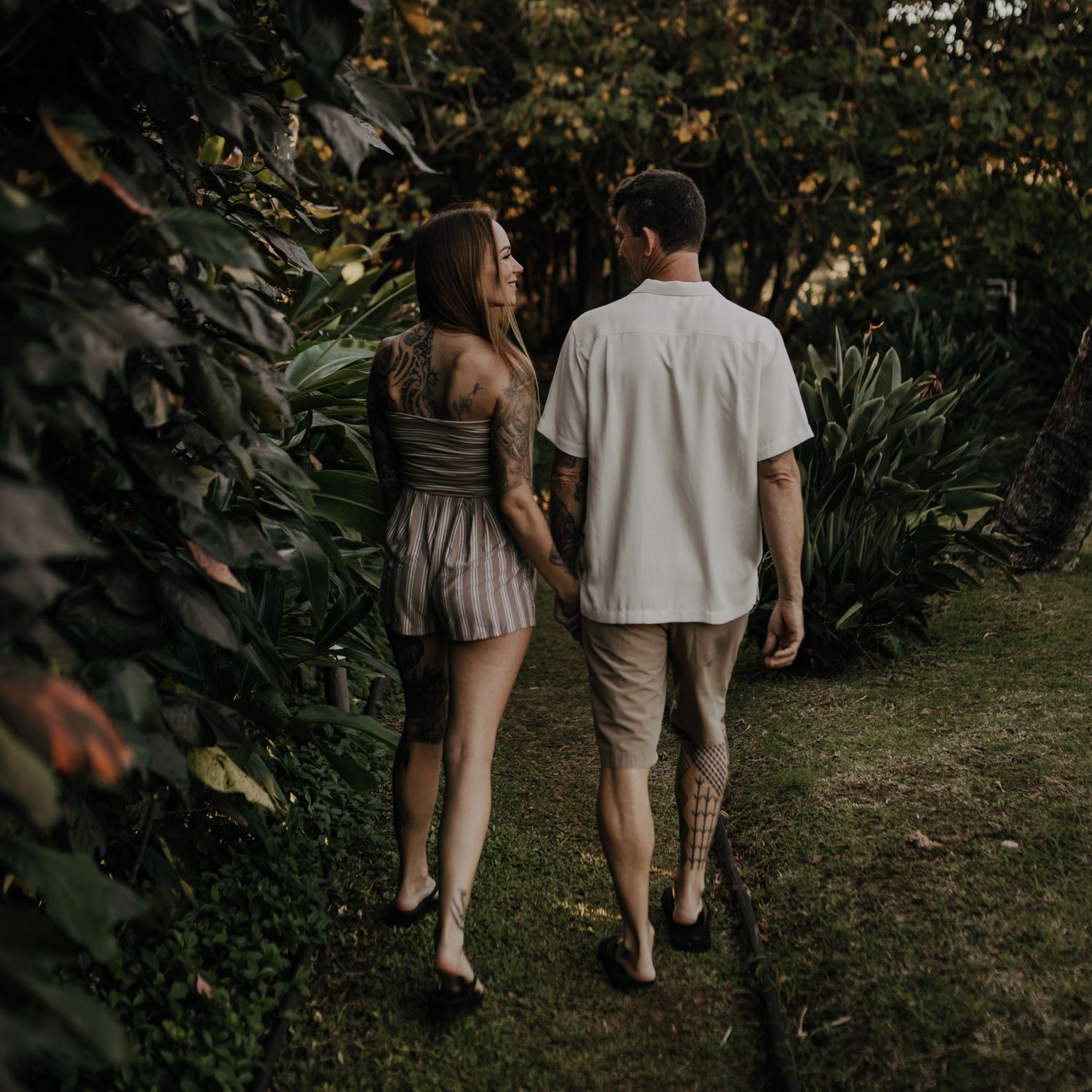 Couple walking together on a garden path surrounded by lush tropical plants and greenery.