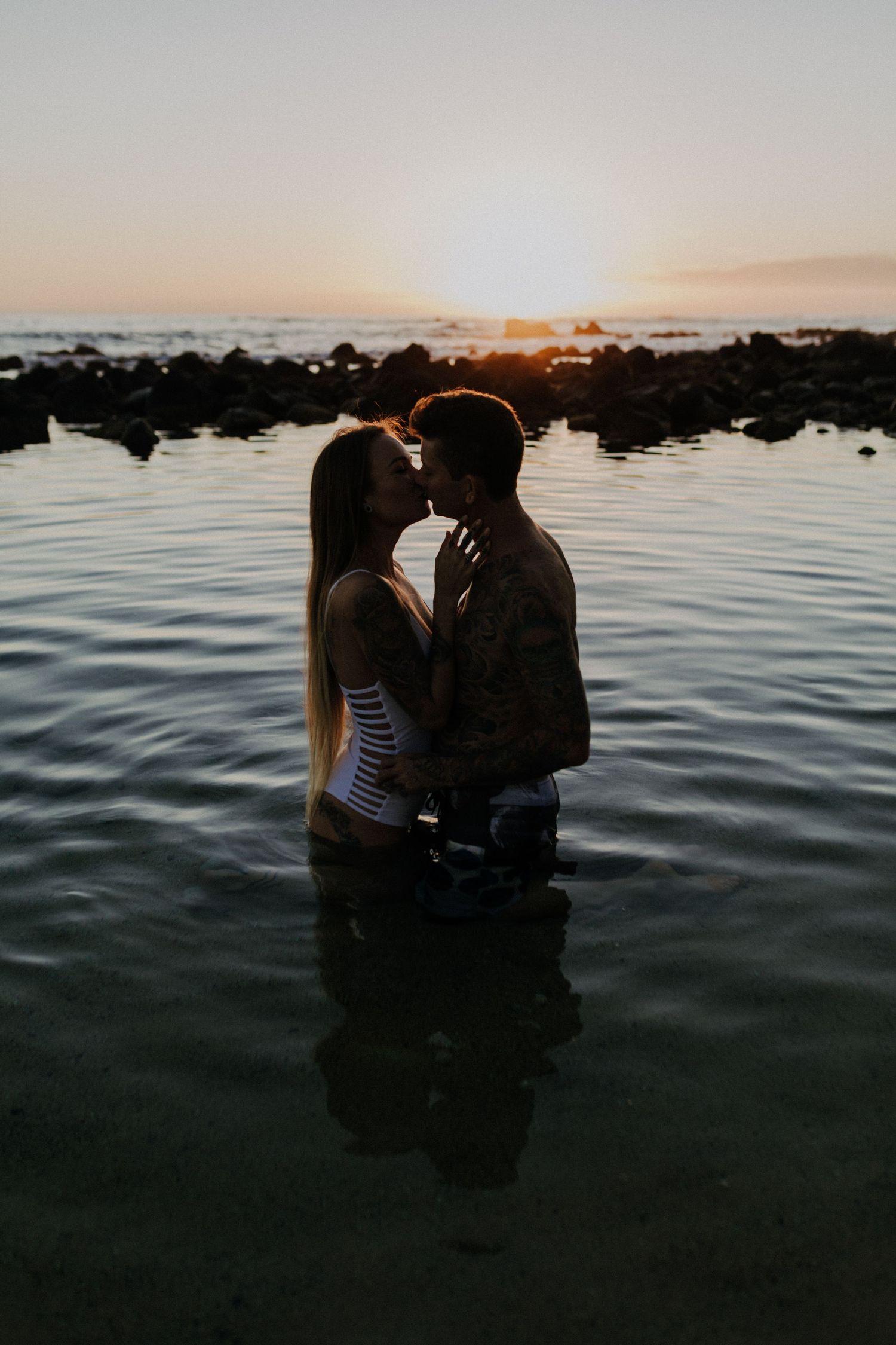 A silhouetted couple embraces in calm waters during sunset, creating a romantic atmosphere.