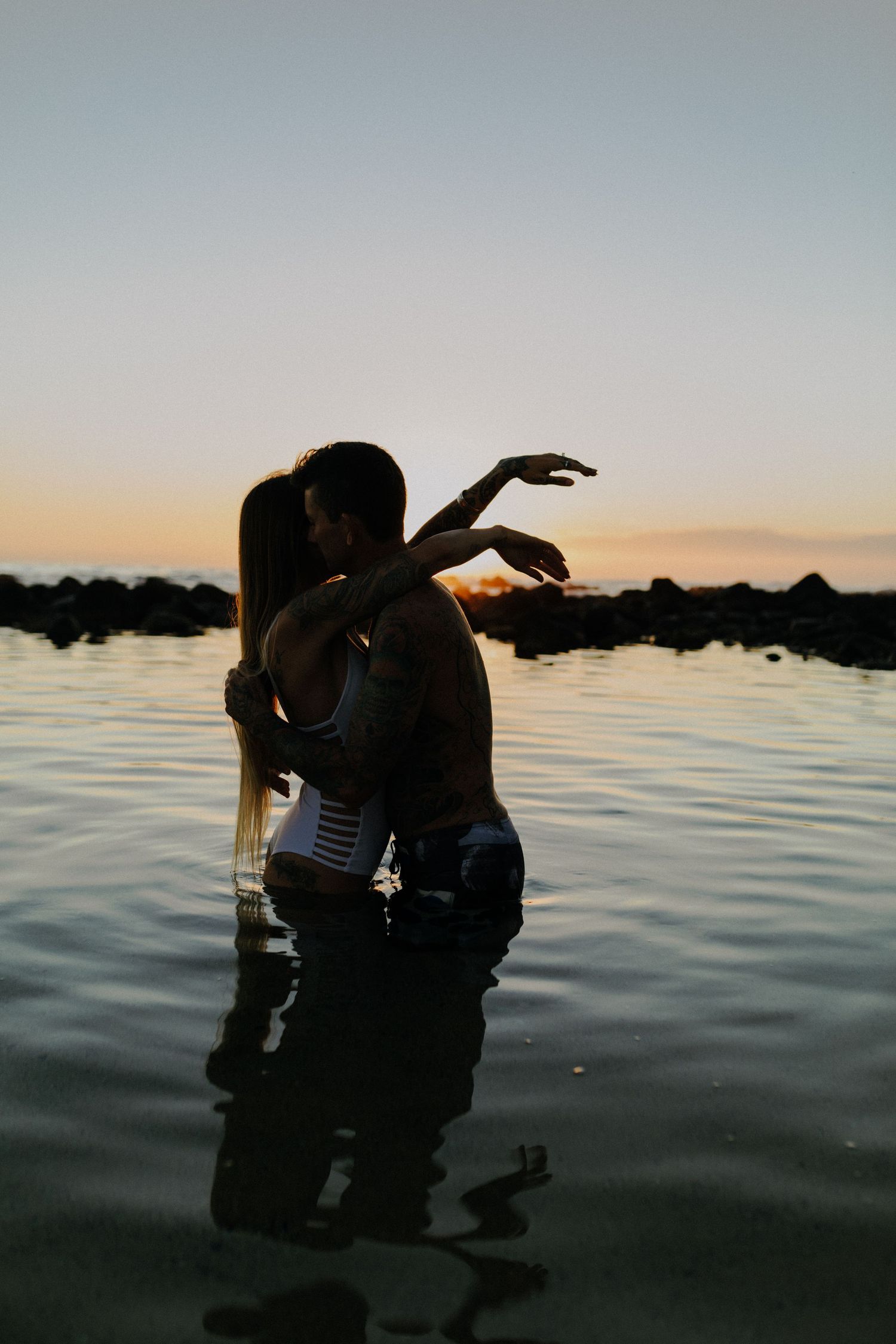 A silhouetted couple embraces in water during sunset, creating a romantic and artistic composition.