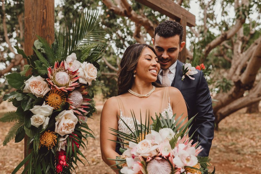 Wedding couple shares tender moments with tropical floral arrangements in an outdoor setting.
