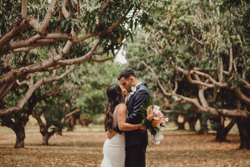 Newlyweds share intimate moments beneath sprawling tree branches in a natural setting.