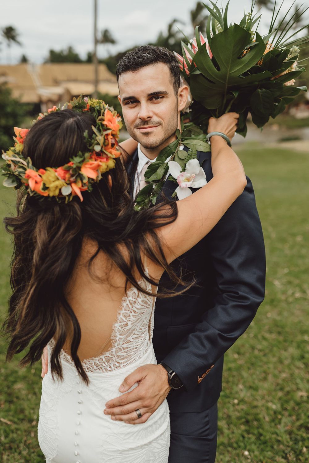 Couple in wedding attire dances on green lawn with tropical flower crown.