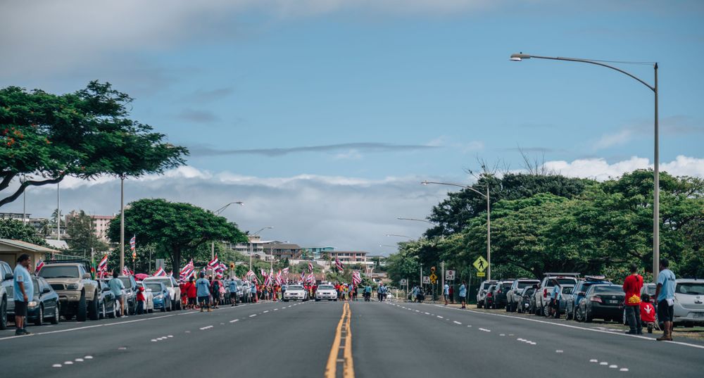 Empty street lined with parked cars and trees under cloudy Hawaiian skies.