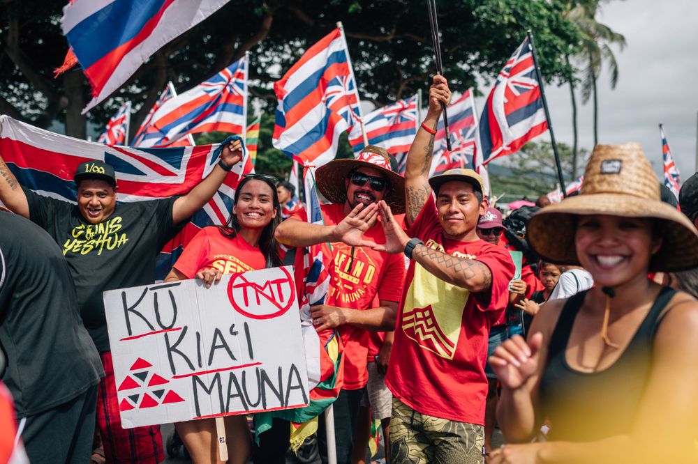 Demonstrators hold signs and Hawaiian flags during a protest rally.