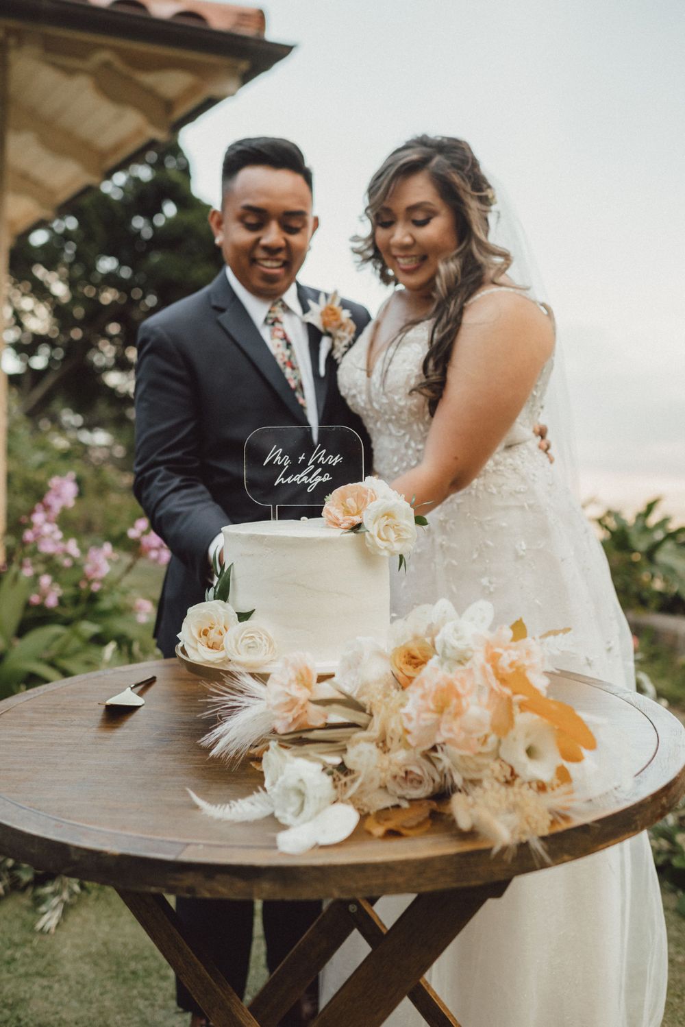 Newlyweds celebrate with traditional cake cutting ceremony at rustic outdoor wedding reception.