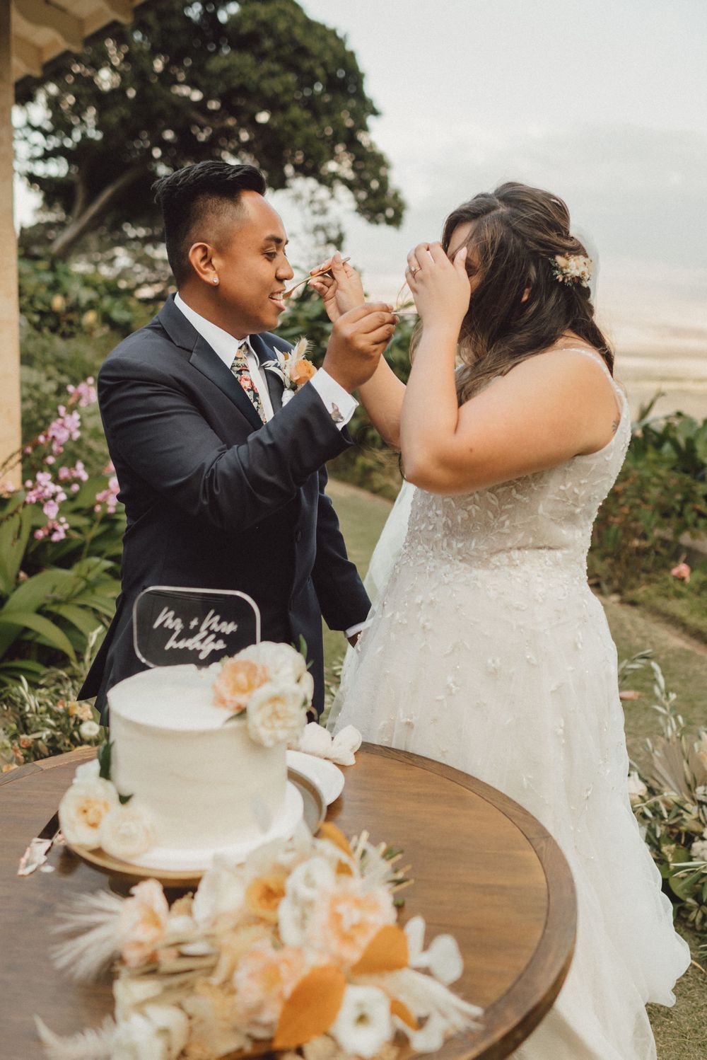 Wedding couple shares intimate cake-cutting moment at outdoor reception with floral decorations.