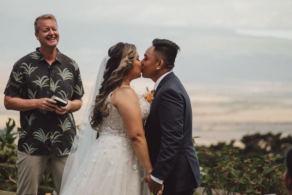 A couple shares their first kiss during an outdoor wedding ceremony.