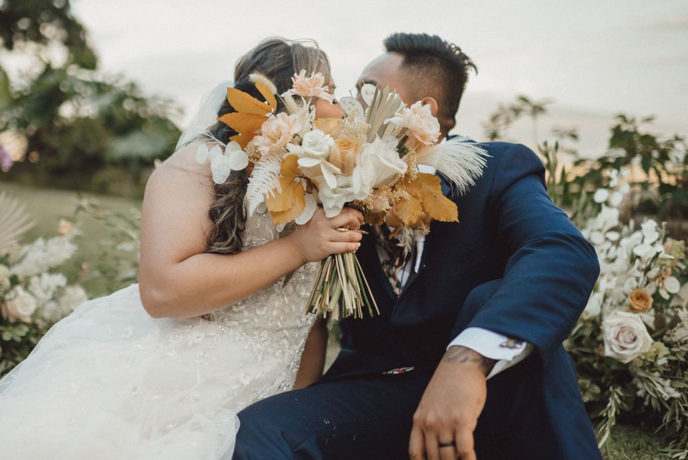 Wedding couple embraces during outdoor celebration with peach and white floral bouquet.