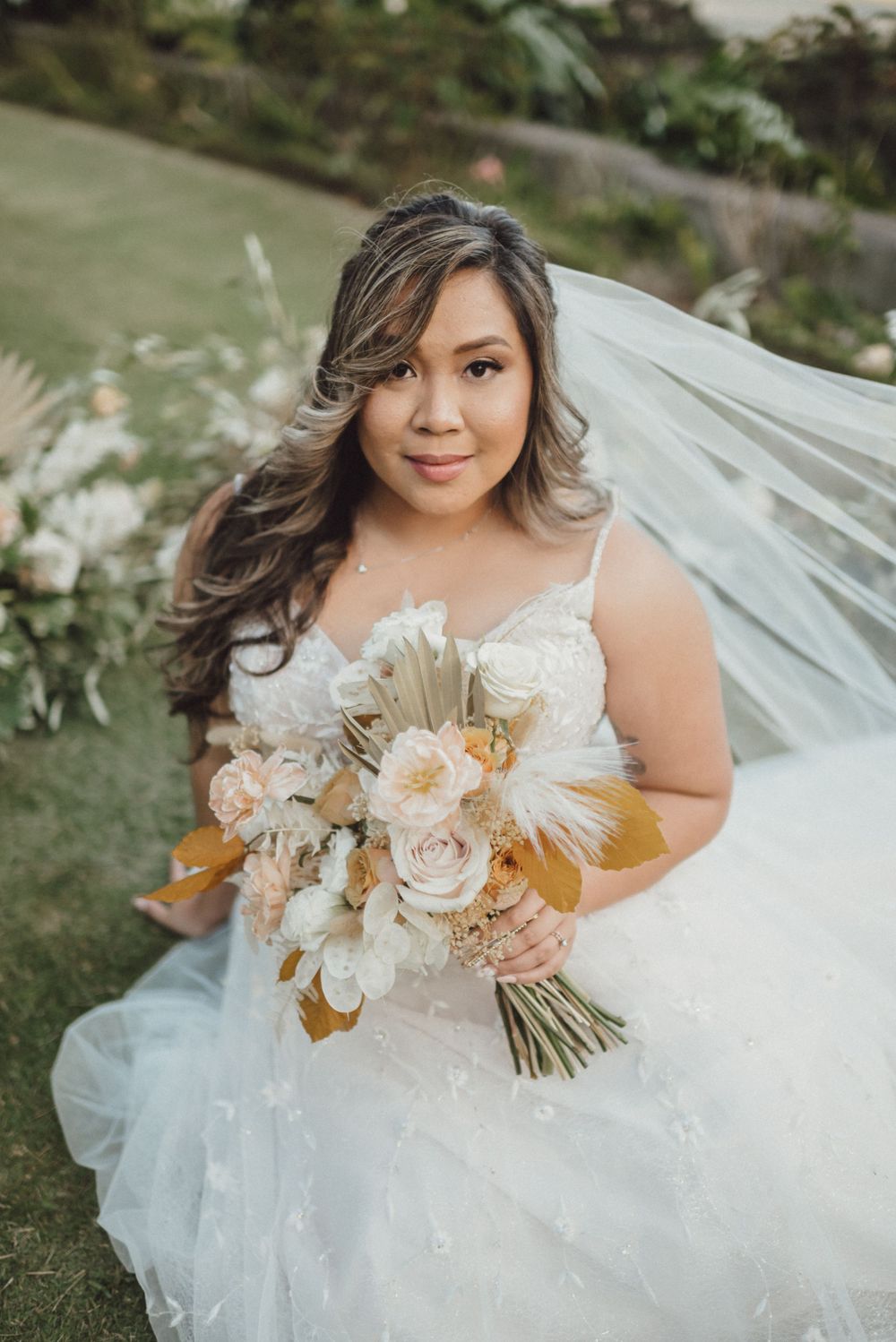 Bride in white lace gown holds elegant peach and cream floral bouquet.