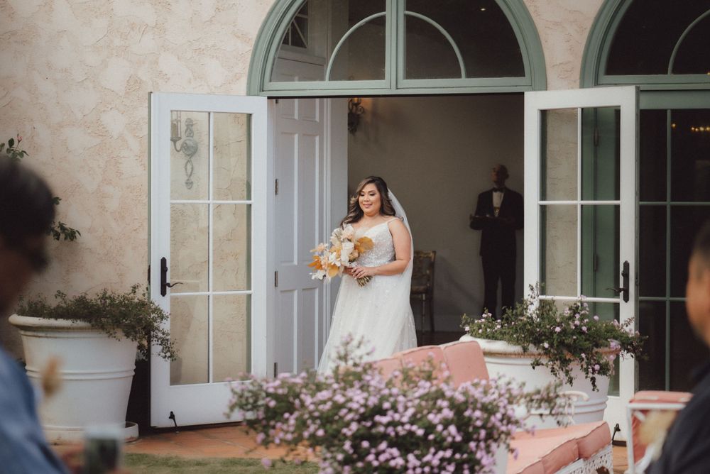 A bride stands in a doorway holding a bouquet at an elegant venue.