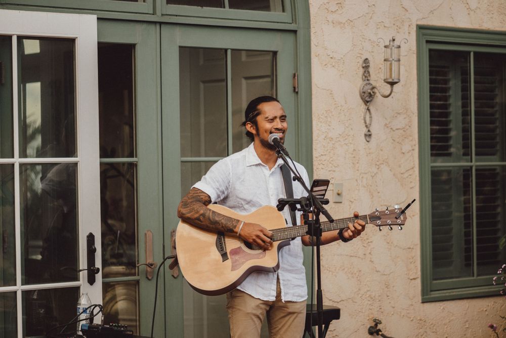 A musician performs with an acoustic guitar outside a building with French doors.