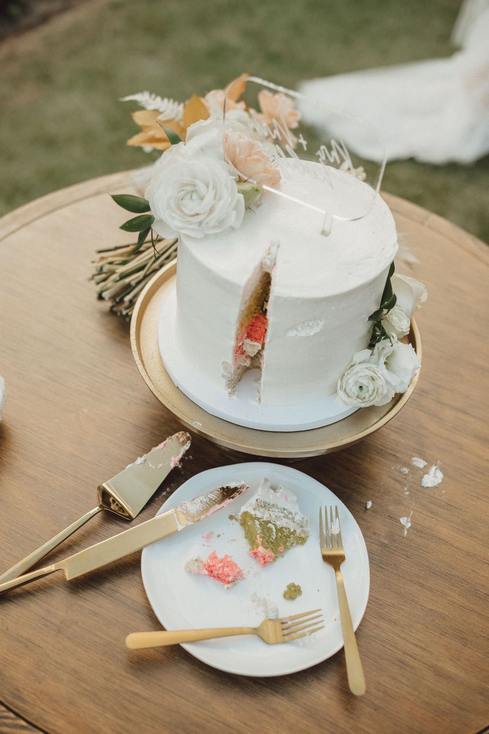 Partially eaten wedding cake and used plates on wooden table with elegant place settings.