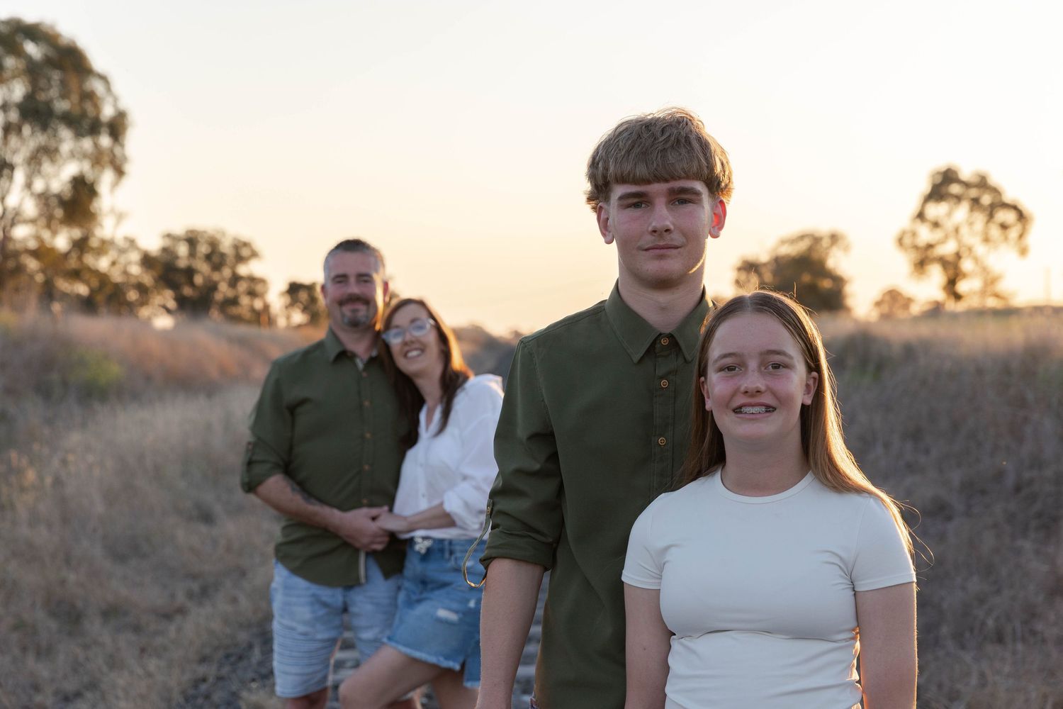 Brother and sister standing in front of their parents at sunset on a railway track for a professional father's day mini photo shoot