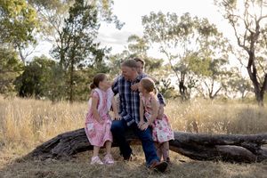 Family sitting on a log in a paddock at sunset during a professional family photo shoot