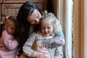 Mum and girls hugging on the floor in the kitchen at family professional photo shoot