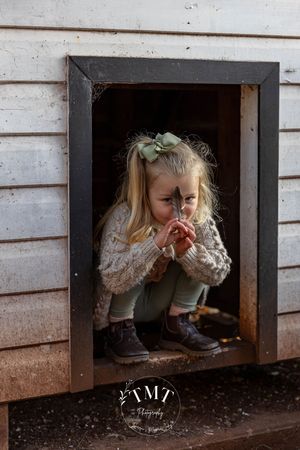 girl holding feather while sitting in chicken coop at family professional photo shoot