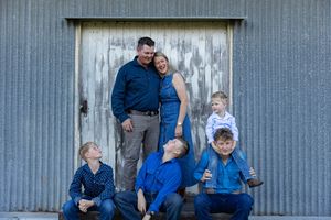 family standing in front of shed on a country rustic farm at family professional photo shoot at sunset