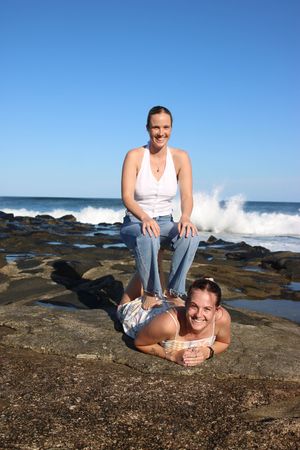 girl sitting on girl's legs at beach