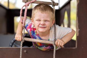 boy with cheeky face looking through a rope ladder in a cubby house