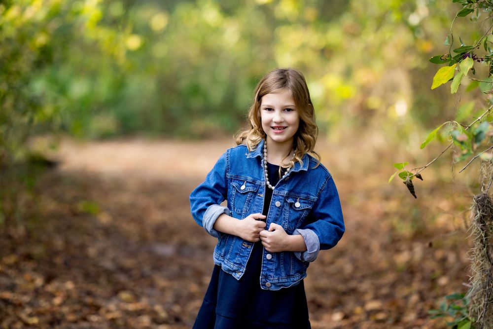 A person in a denim jacket poses outdoors among autumn leaves and natural scenery.