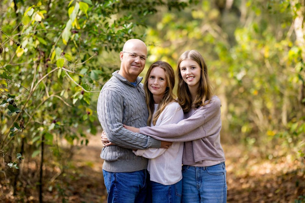 A family embraces warmly while standing together in a sunlit autumn forest setting.