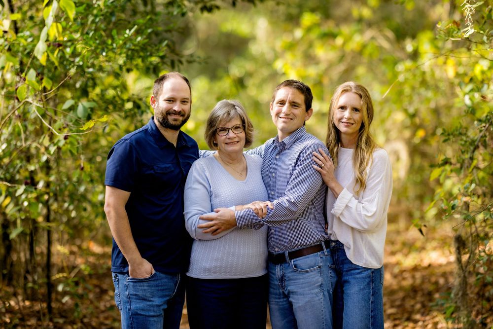 A group poses together outdoors on a sunny autumn day surrounded by green and yellow foliage.