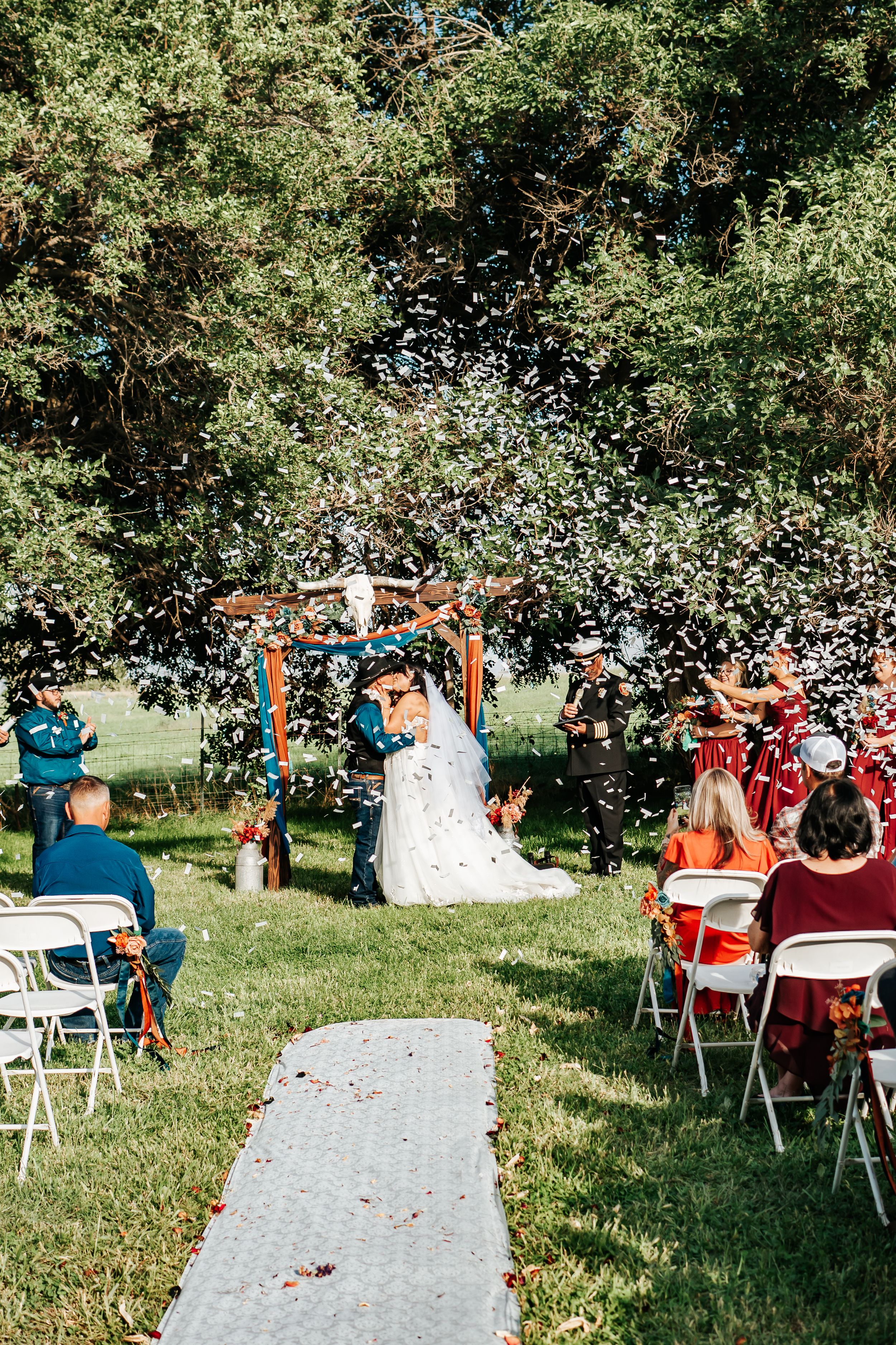 Wedding guests toss confetti in celebration at an outdoor ceremony at a Eastern Oregon wedding ceremony in a green pasture.