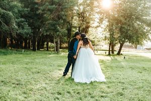 Couple in wedding attire walking together through a sunlit park during golden hour.