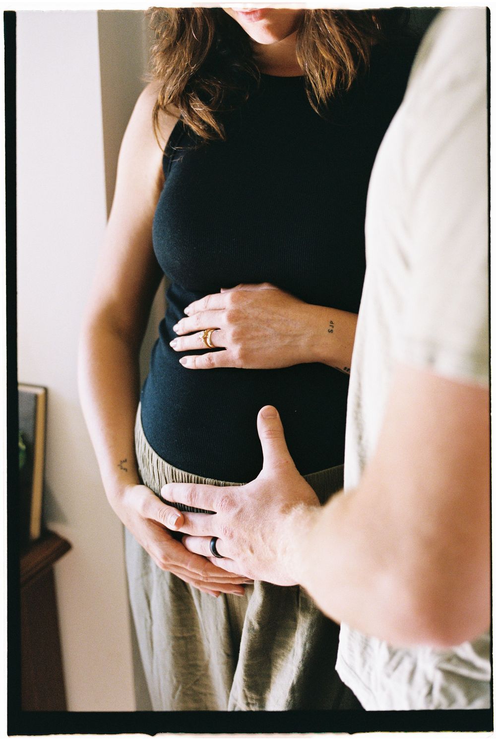 A series of intimate maternity photos showing hands gently cradling a pregnant belly in a black top and grey pants.