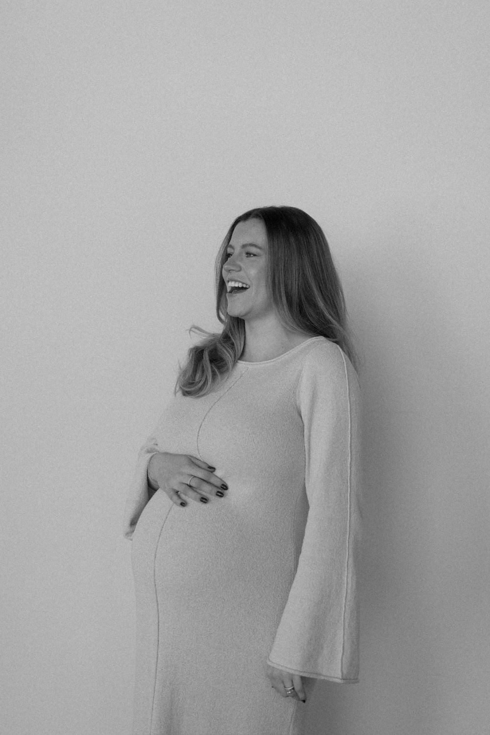 Black and white photo series showing a person in a light colored sweater laughing joyfully against a plain wall.