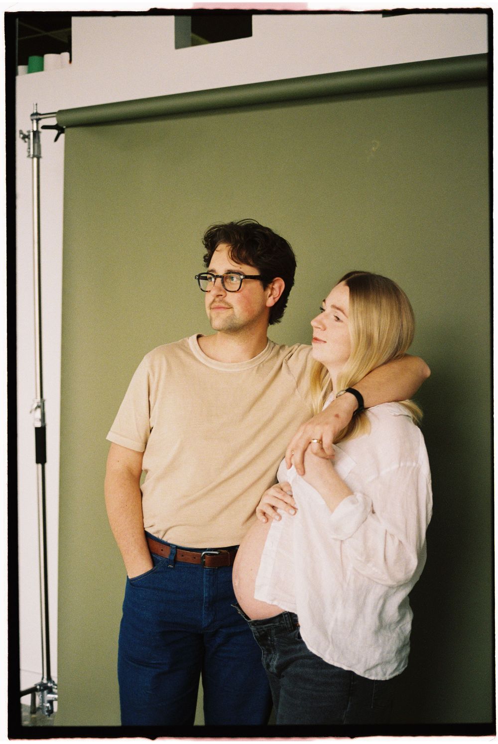 A couple in casual attire poses against a green wall in a series of intimate candid shots.
