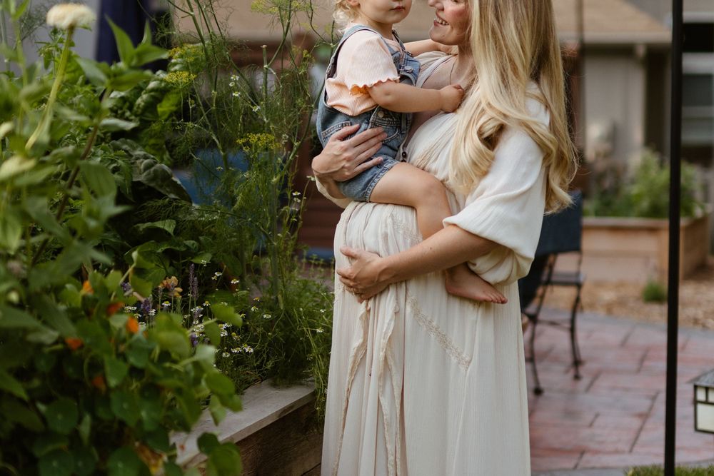 A tender moment captured in a garden setting with white flowing dresses and natural greenery surroundings.