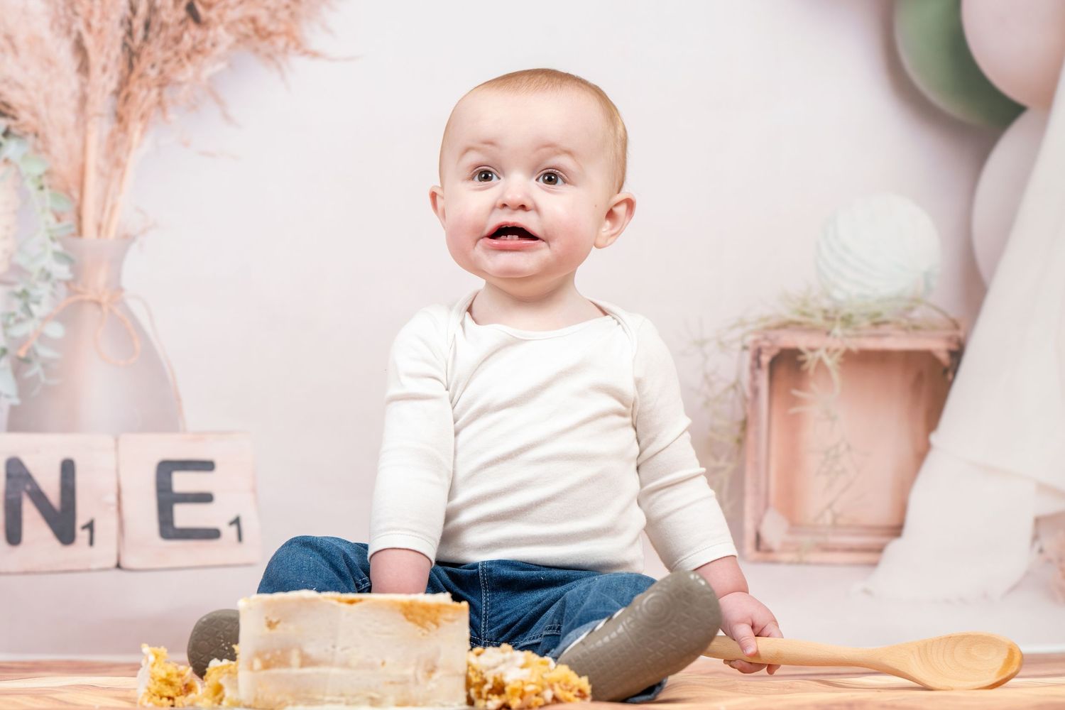 Baby in white shirt sits on floor playing with colorful wooden alphabet blocks and toys.