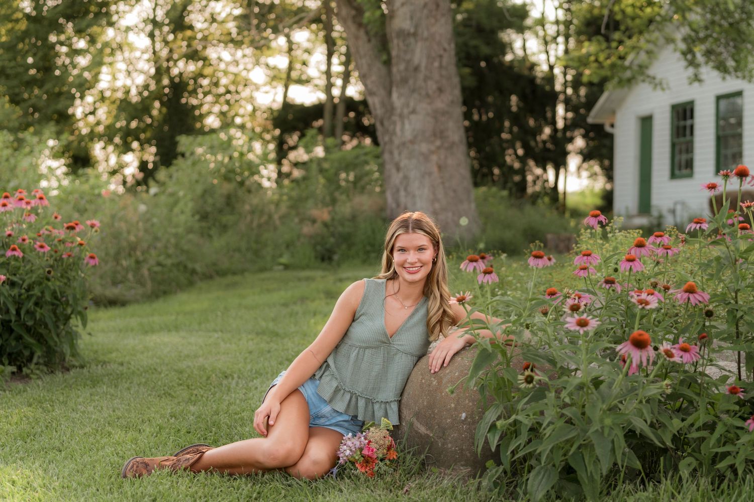 A person sits cross-legged in a summer meadow with tall grass and wildflowers during golden hour.
