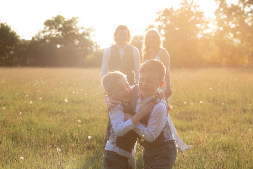 Family group playing and embracing in a sunlit summer field at sunset.