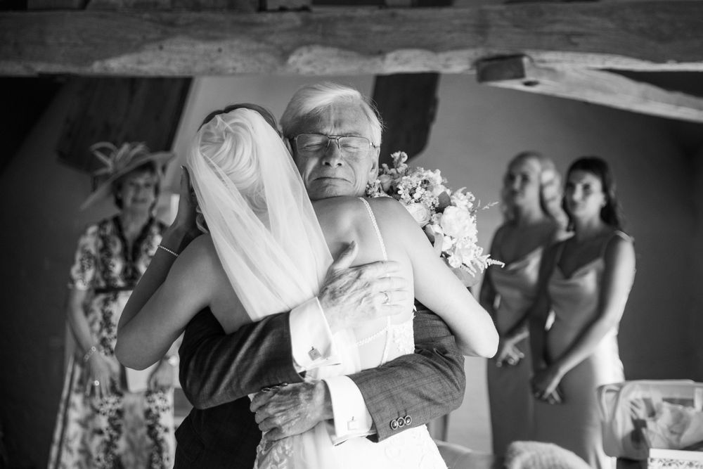 Black and white photo of an emotional wedding embrace with guests in the background.