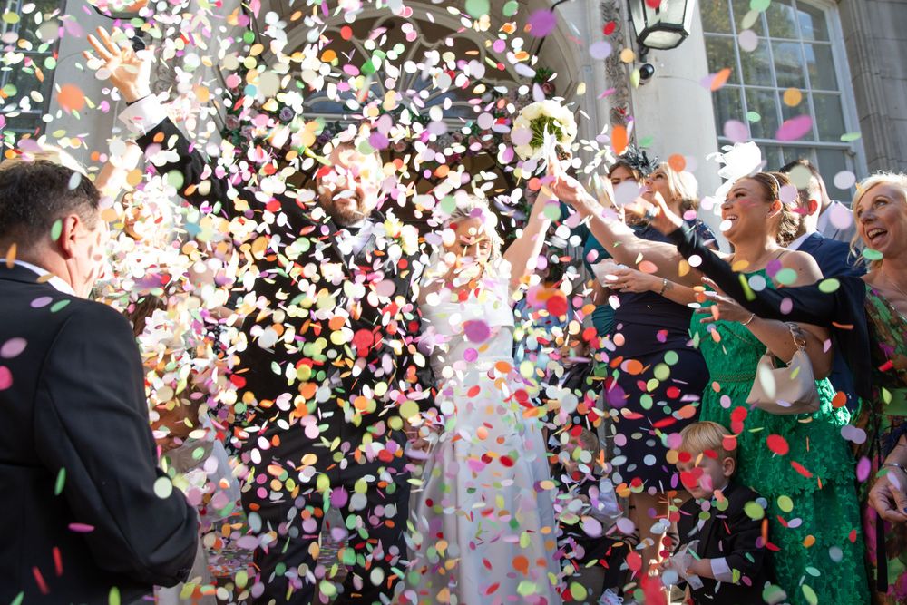 Wedding guests throw colorful confetti during a celebratory moment at an outdoor ceremony.