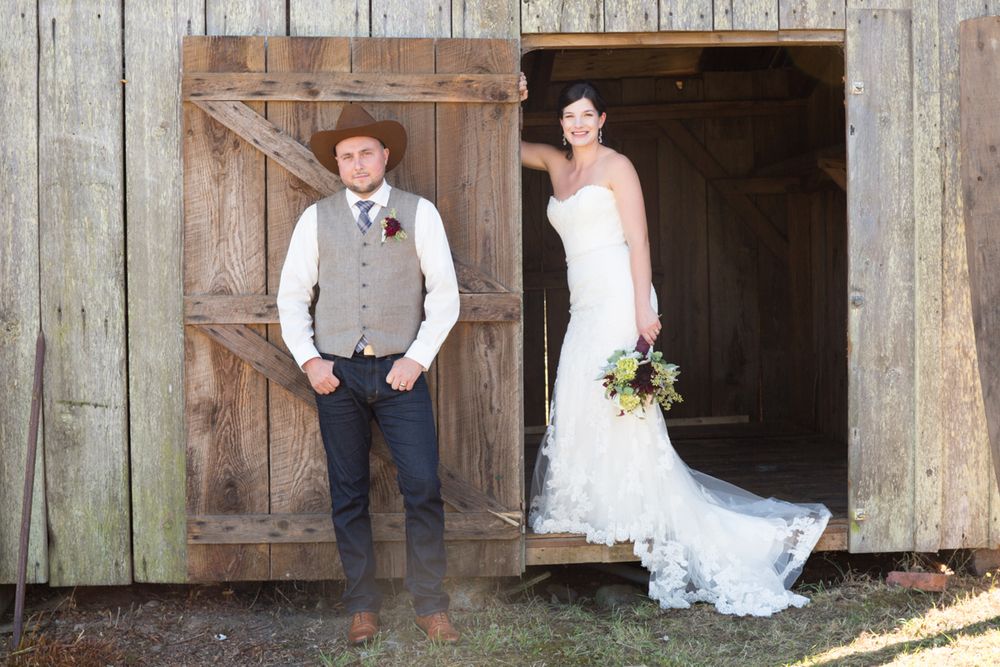 Two people pose in a rustic barn doorway during a country-themed wedding portrait.