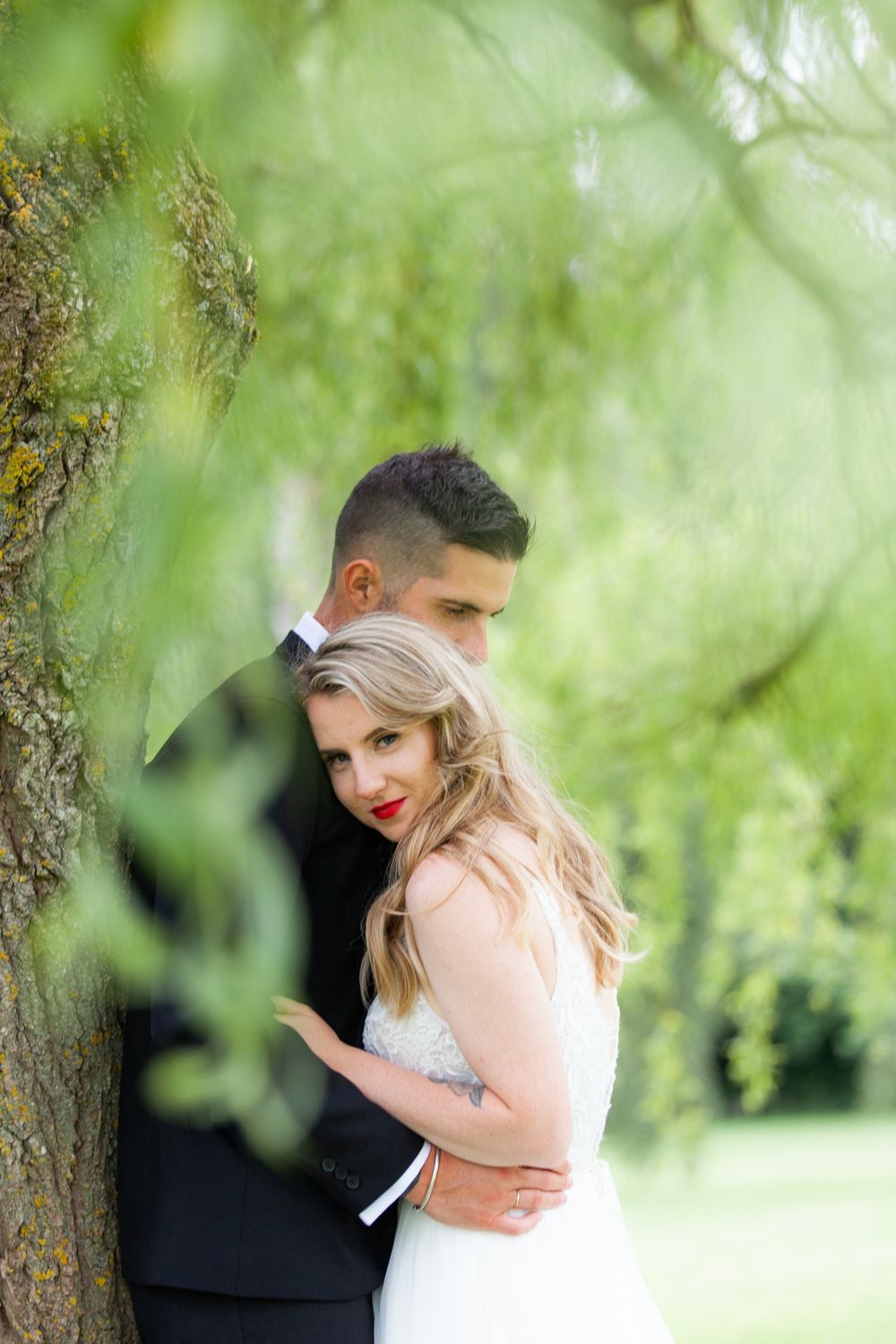 Intimate portrait of couple embracing against soft green foliage background.