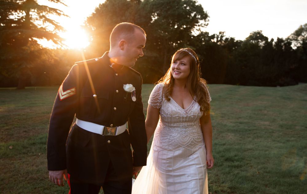 A sunset wedding portrait featuring a military groom and bride in a lace dress against a golden field.