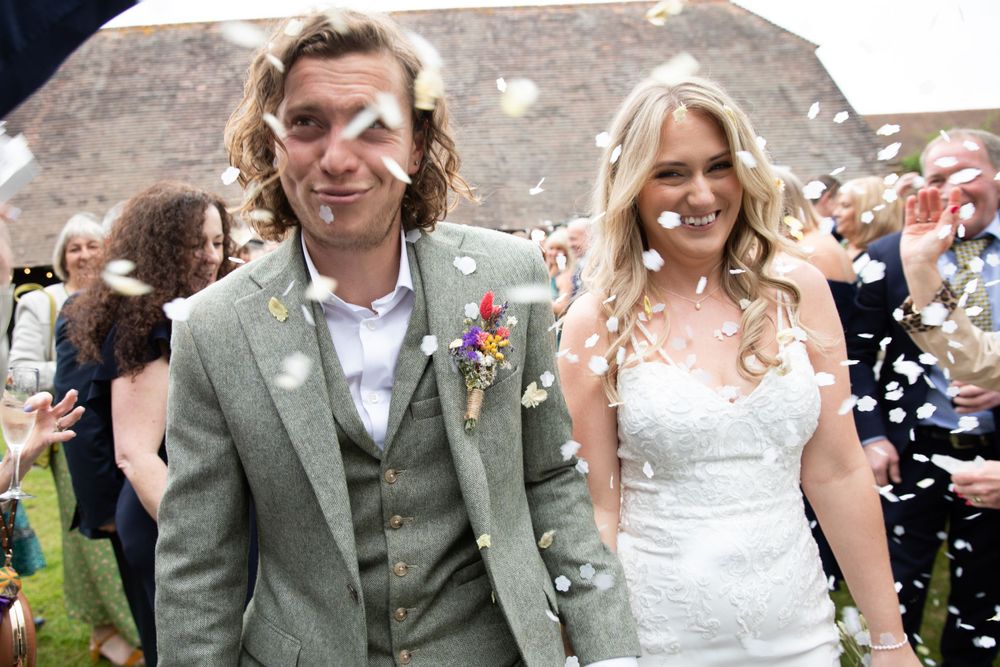 Newlyweds walking through shower of confetti after outdoor wedding ceremony.