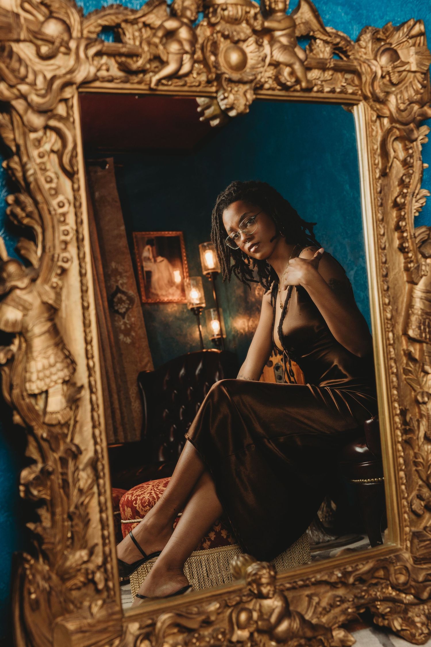 A moody reflection in an ornate gold mirror shows a figure in dim lighting creating an artistic composition.