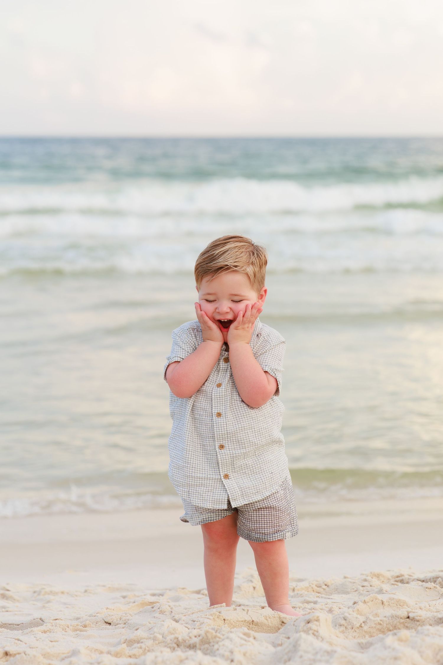 Small child plays on sandy beach at sunset wearing light colored clothing near ocean waves.