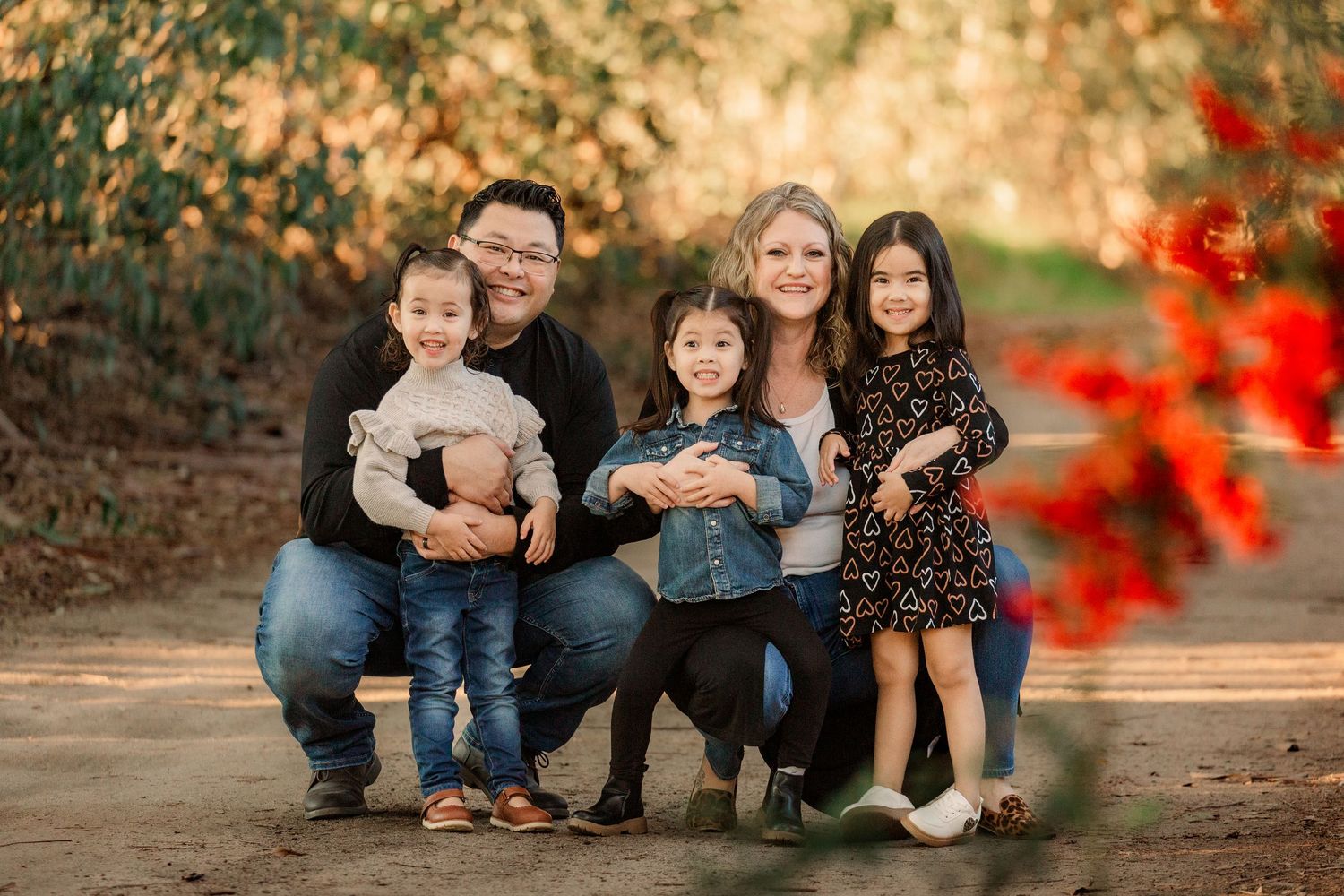 Family wearing coordinating blue outfits sits together on fallen autumn leaves in an outdoor setting.